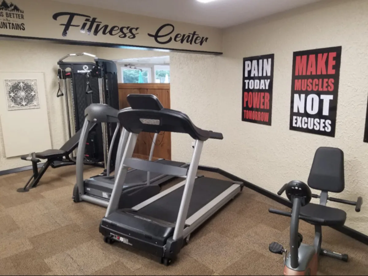 A bright, modern fitness room featuring a treadmill, exercise bike, weight machine, and motivational posters on the wall. Large mirrors and an open layout invite guests to enjoy personal fitness routines or group workouts.