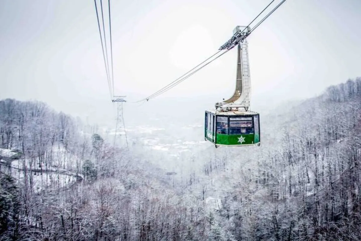 A gondola glides above snow-covered trees and rolling mountain slopes, offering panoramic views of the majestic Smoky Mountains and the valley below. The scene captures both adventure and tranquility in a single frame.