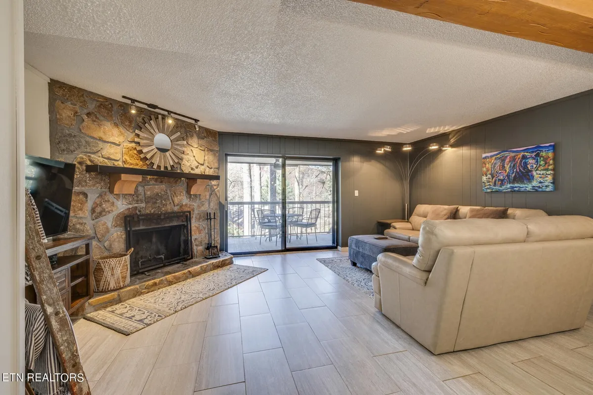 A spacious living room featuring a prominent stone fireplace, large windows framing breathtaking views of the Great Smoky Mountains, and a cozy, comfortable seating arrangement perfect for gatherings.
