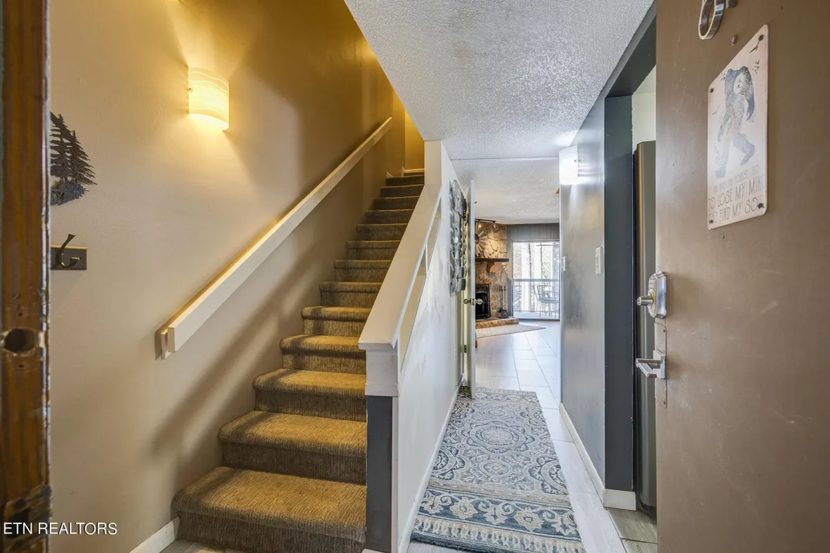 The image showcases the inviting entryway of a spacious, modern condo, featuring a striking staircase, tasteful wall art, and a cozy rug. The atmosphere is warm and welcoming, hinting at comfortable family gatherings and easy access to all areas of the home.