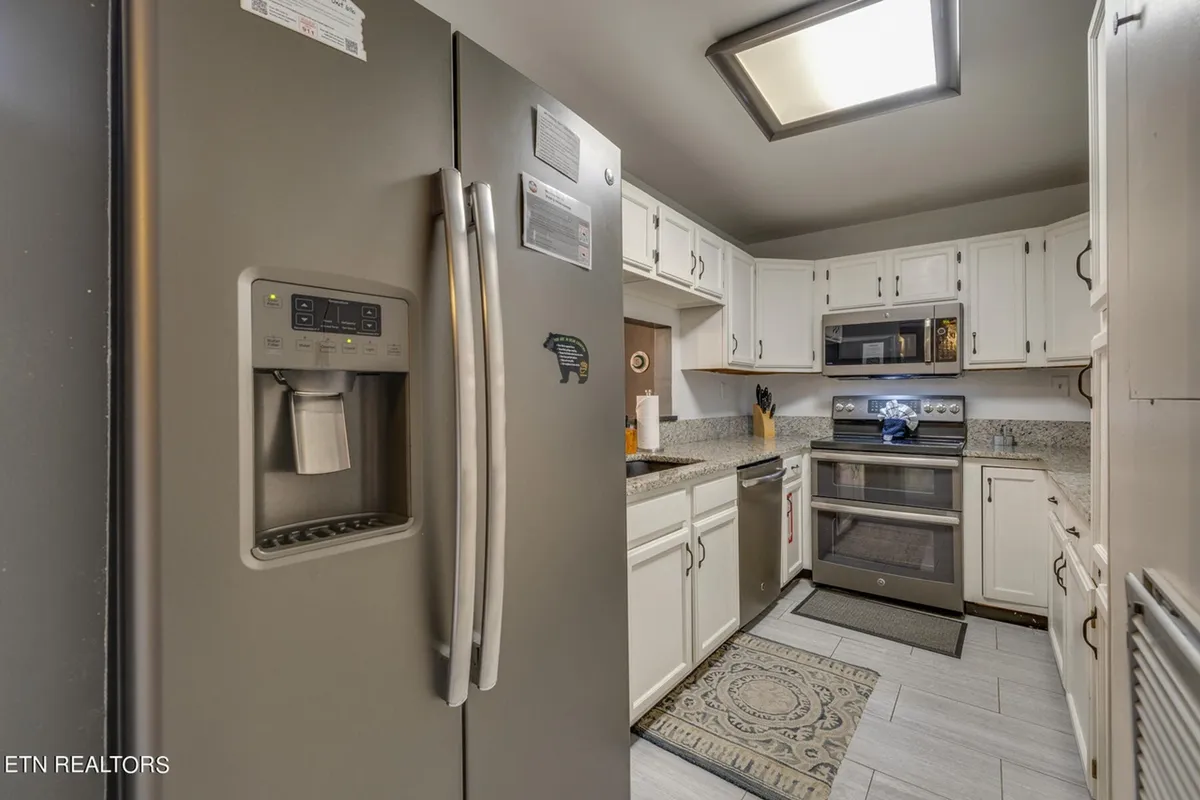 A bright, modern kitchen featuring stainless steel refrigerator, oven, and microwave, with expansive granite countertops and a cozy kitchen rug. The room includes ample workspace and a welcoming ambiance, perfect for preparing meals and gathering around the island.
